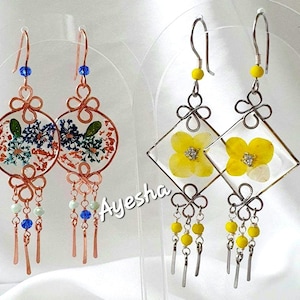 May include: Two pairs of dangle earrings. The left pair features copper-toned circular frames with pressed blue and green flowers, blue beads, and copper dangles. The right pair features silver-toned diamond frames with yellow flowers and yellow beads.