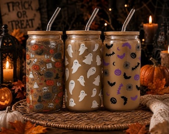 May include: Three clear glass tumblers with bamboo lids and glass straws. The first features orange and black Halloween icons, the second has white ghost silhouettes, and the third displays purple and black bats, spiders, and pumpkins.