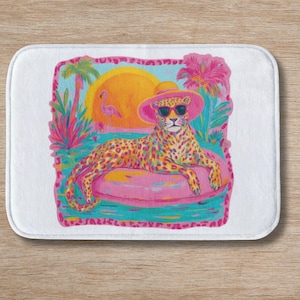 May include: A rectangular bath mat featuring a colorful illustration of a leopard wearing a pink sun hat and black sunglasses while lounging on a pink inflatable pool float. The scene includes a bright yellow sun, a pink flamingo, and palm trees.