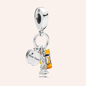 Può includere: Un charm in argento con tre ciondoli: un'etichetta a forma di mela con la scritta "New York", una Statua della Libertà e un taxi giallo. Il charm ha un anello nella parte superiore per l'attacco.