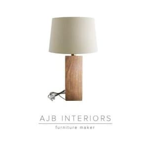 May include: A wooden table lamp with a beige lampshade. The lamp has a square base and a simple design.