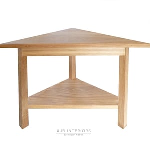 May include: A triangular wooden corner table with a lower shelf. The table is made of light wood and has a simple, modern design.