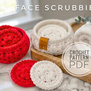Puede incluir: Se muestran esponjas faciales y una cesta de ganchillo rojas y blancas. El texto "FACE SCRUBBIES" está en la parte superior. También se ven una toalla blanca y una pequeña botella de aceite. La imagen también incluye un gráfico "CROCHET PATTERN PDF".