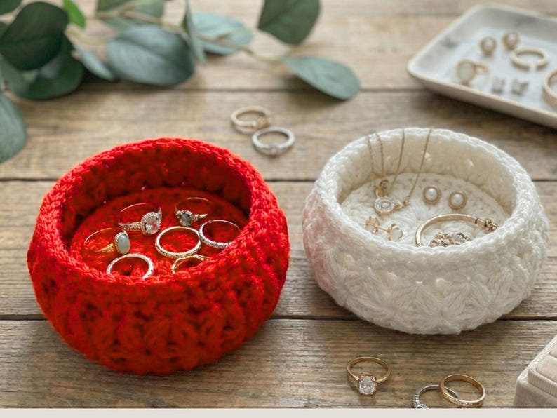 Peut inclure: Deux bols ronds crochet&eacute;s &agrave; la main pour le rangement de bijoux, l'un rouge vif et l'autre blanc cass&eacute;. Le bol rouge contient plusieurs bagues en or et argent avec diverses pierres. Le bol blanc contient des colliers, boucles et bracelets.