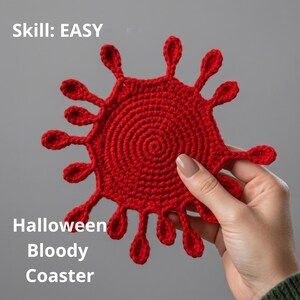 Könnte beinhalten: Ein leuchtend roter gehäkelter Untersetzer mit einer kreisförmigen Mitte und mehreren strahlenförmigen, blütenblattartigen Fortsätzen. Der Text "Skill: EASY" und "Halloween Bloody Coaster" ist auf dem Bild zu sehen. Das Objekt ist aus Garn.