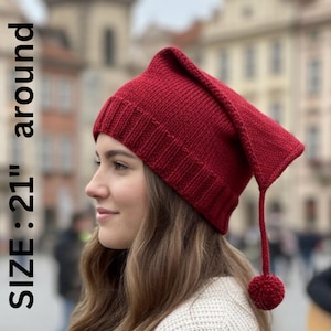 May include: A knitted red hat with a pointed top and a dangling tassel ending in a pom-pom. The hat is approximately 21 inches around. The hat is made of a textured knit material.