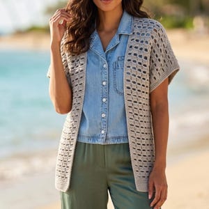 May include: A beige open-front crochet cardigan with short sleeves and a repeating rectangular grid pattern. The garment is layered over a light blue button-down denim shirt and olive green trousers, creating a textured and layered appearance.