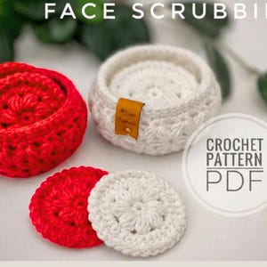 Peut inclure: Deux paniers ronds au crochet, un rouge et un blanc, contenant chacun des disques d&eacute;maquillants assortis. Chaque panier poss&egrave;de une petite &eacute;tiquette en cuir beige marqu&eacute;e Love Handmade. Le texte FACE SCRUBBIES et CROCHET PATTERN PDF est visible.