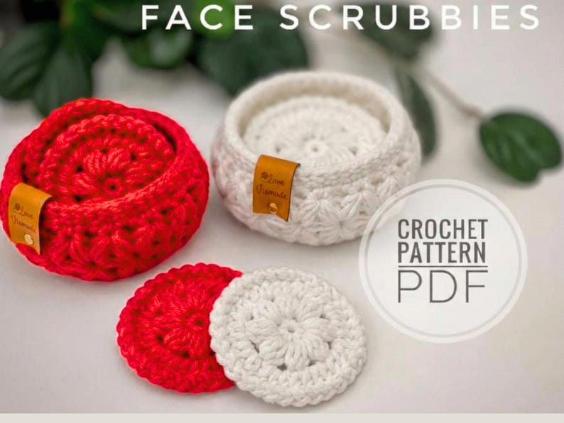 Peut inclure: Deux paniers ronds au crochet, un rouge et un blanc, contenant chacun des disques d&eacute;maquillants assortis. Chaque panier poss&egrave;de une petite &eacute;tiquette en cuir beige marqu&eacute;e Love Handmade. Le texte FACE SCRUBBIES et CROCHET PATTERN PDF est visible.
