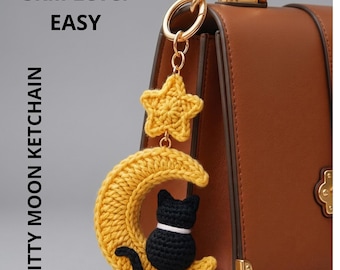 Peut inclure: Un porte-clés en crochet composé d'une étoile jaune et d'un croissant de lune jaune avec un petit chat noir assis dessus. Le porte-clés est attaché à un sac à main marron avec des détails dorés. Le texte indique : Skill Level EASY KITTY MOON KETCHAIN.