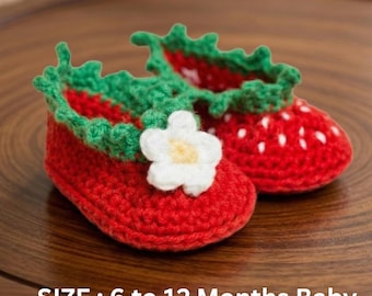 Peut inclure: Une paire de chaussons pour bébé en crochet rouge, en forme de fraises. Bordure verte et fleur blanche. Le texte "SIZE : 6 to 12 Months Baby" est visible.