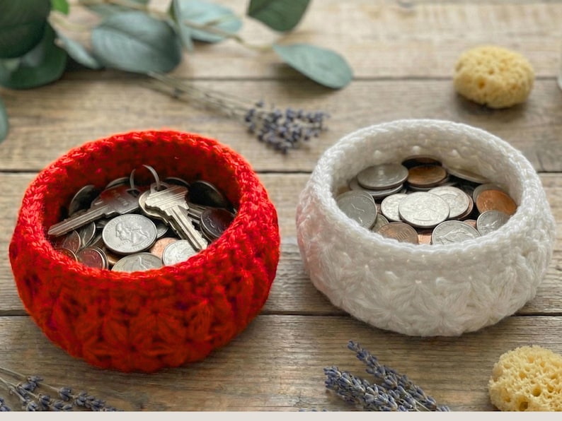 Peut inclure: Deux bols ronds crochet&eacute;s &agrave; la main avec un motif textur&eacute; en forme d'&eacute;toile. Le bol de gauche est rouge vif et contient un ensemble de cl&eacute;s en m&eacute;tal et de pi&egrave;ces de monnaie. Le bol de droite est blanc et rempli de pi&egrave;ces en argent et en cuivre.
