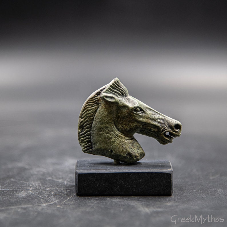 May include: A bronze horse head sculpture on a black base. The horse's head is facing to the right and has a detailed mane.