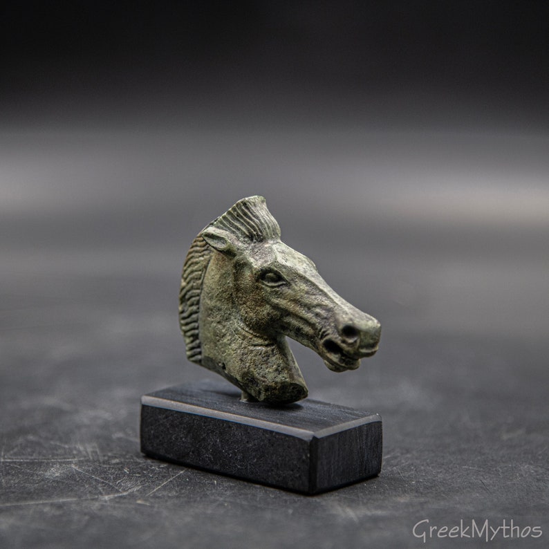 May include: A bronze horse head sculpture on a black wooden base. The sculpture is detailed and has a green patina.