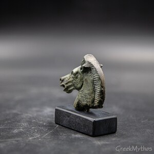 May include: A bronze horse head sculpture on a black wooden base. The sculpture is detailed and has a green patina.