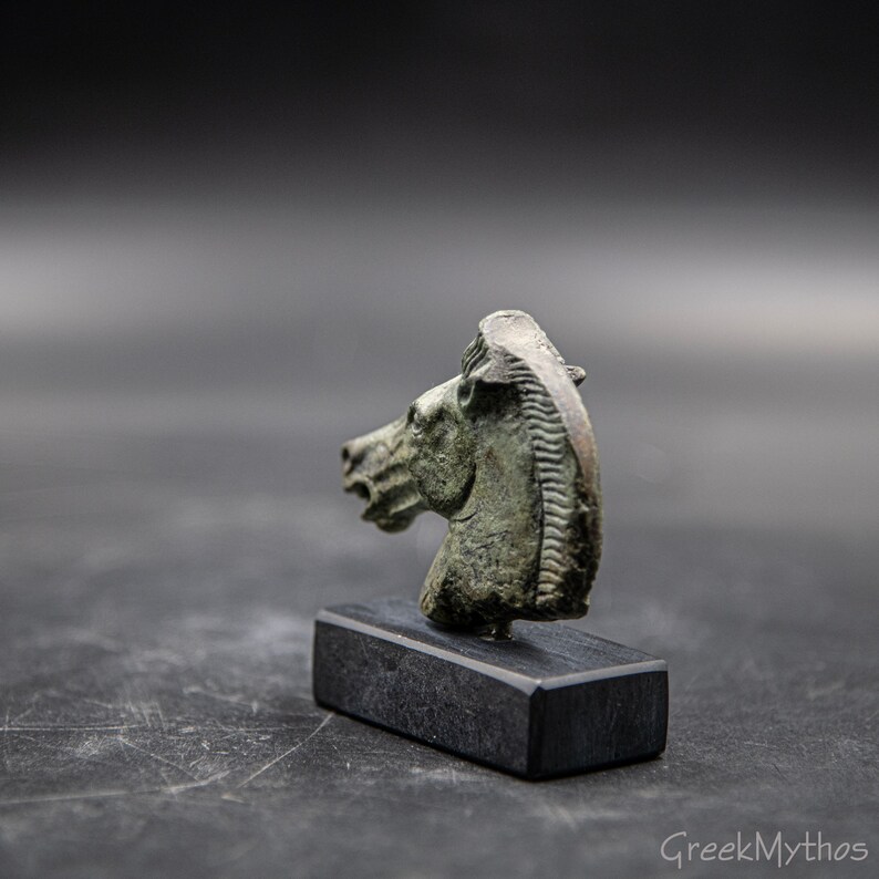 May include: A bronze horse head sculpture on a black wooden base. The sculpture is detailed and has a green patina.