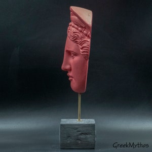 May include: A red painted plaster bust of a woman's face on a black wooden base with a gold metal stand. The bust is broken and only the face and top of the head are present. The woman is wearing a crown.
