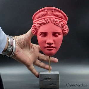 May include: A red painted plaster bust of a woman's head with a crown of peacocks on top. The bust is on a black wooden stand.