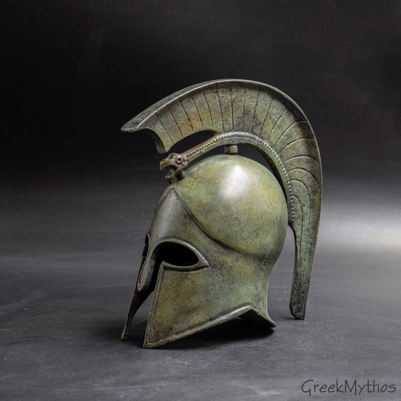 May include: A bronze Greek warrior helmet with a plume on top. The helmet has a detailed design and a weathered finish.