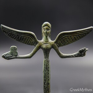 May include: A bronze statue of a winged figure with an owl on one outstretched arm and a hand outstretched on the other arm. The figure is standing on a base with a decorative pattern.