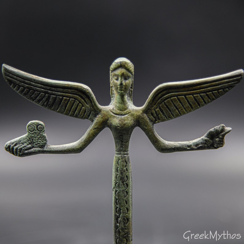 May include: A bronze statue of a winged figure with an owl on one outstretched arm and a hand outstretched on the other arm. The figure is standing on a base with a decorative pattern.