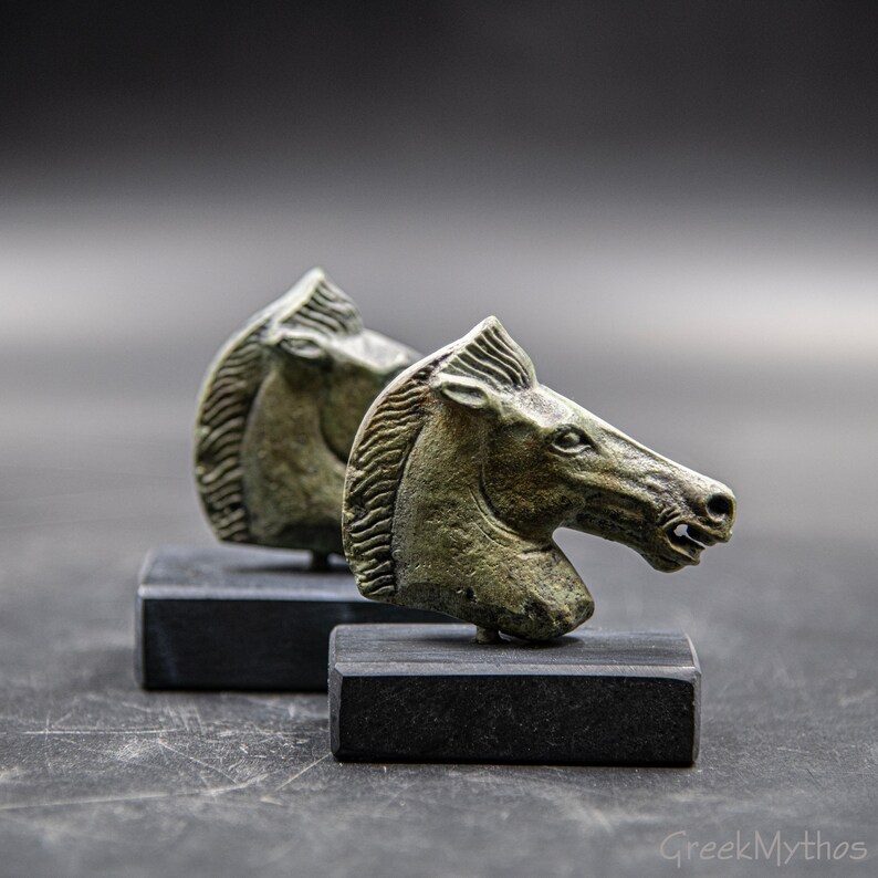 May include: Two bronze horse head sculptures on black bases. The sculptures are detailed and have a green patina.