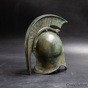 May include: A bronze Greek warrior helmet with a crested plume and a serpent design on the top. The helmet is weathered and has a green patina.
