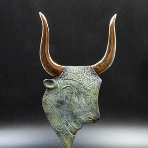 May include: A bronze bull's head sculpture with gold horns. The bull's head is detailed with intricate patterns and textures.