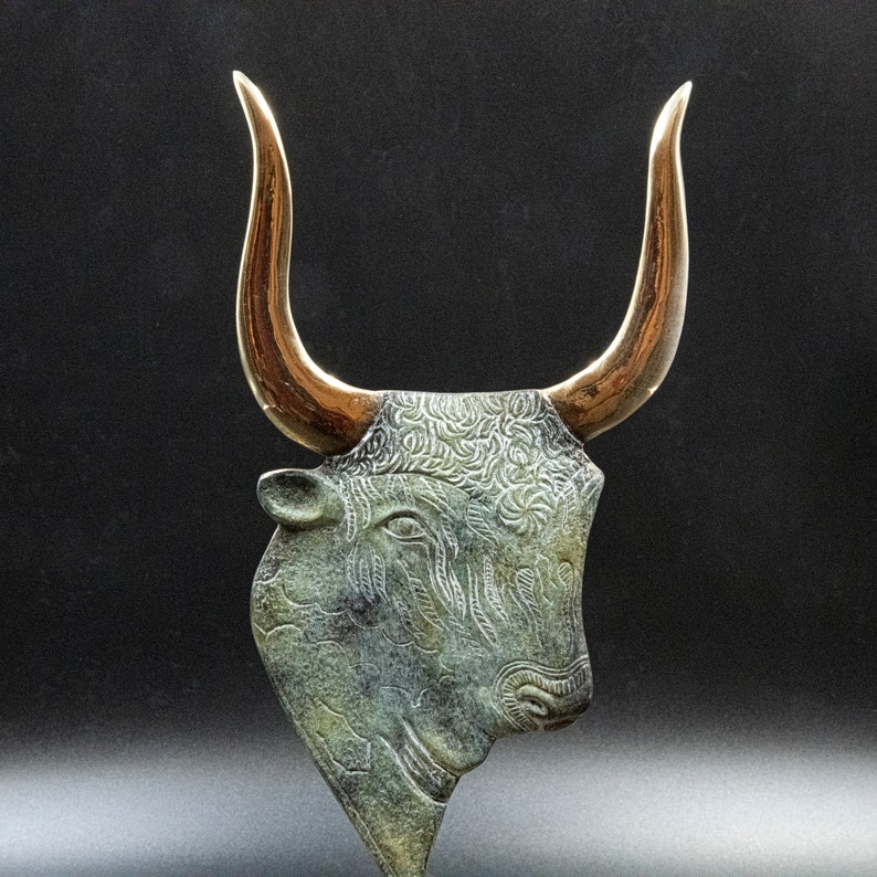 May include: A bronze bull's head sculpture with gold horns. The bull's head is detailed with intricate patterns and textures.