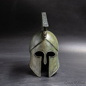May include: A bronze Greek warrior helmet with a plume on top. The helmet has a distinctive design with a pointed crest and a face mask.