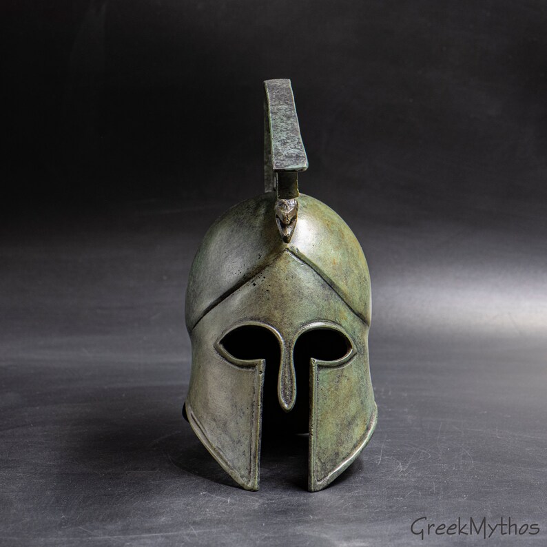 May include: A bronze Greek warrior helmet with a plume on top. The helmet has a distinctive design with a pointed crest and a face mask.