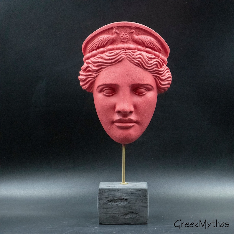 May include: A red painted plaster bust of a woman's head with a crown of birds on top. The bust is on a black wooden base with a gold metal rod.