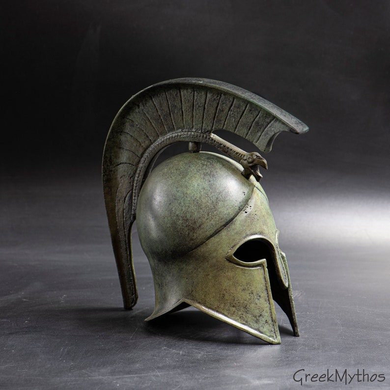 May include: A bronze Greek warrior helmet with a plume and a crest in the shape of a bird's head. The helmet is weathered and has a green patina.