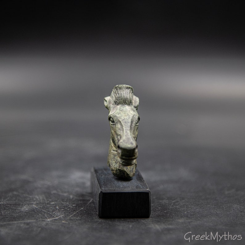 May include: A bronze horse head sculpture on a black stand. The sculpture is a detailed depiction of a horse's head with a mane and a bridle.