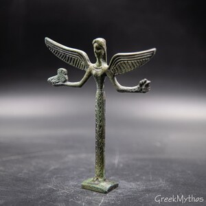 May include: A bronze statue of a winged figure with four arms. The figure is holding an owl in one hand and a flower in another. The statue is standing on a square base.