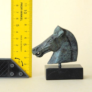 May include: A bronze horse head sculpture on a black marble base. The sculpture is about 5 inches tall and is a detailed representation of a horse's head.