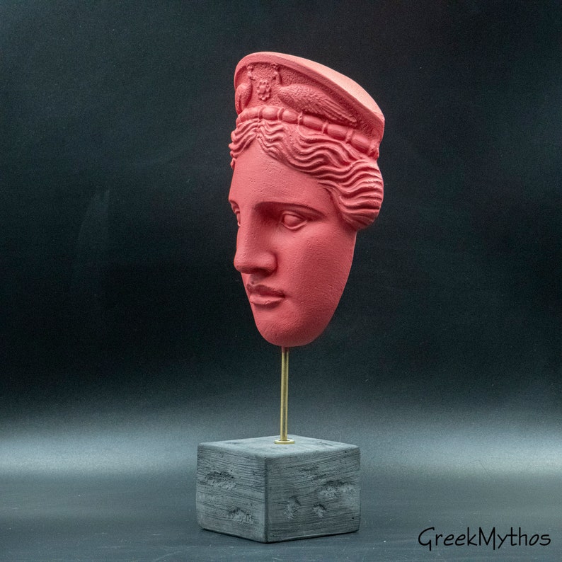 May include: A red painted plaster bust of a woman with a crown on her head. The bust is on a black square base with a gold metal rod.