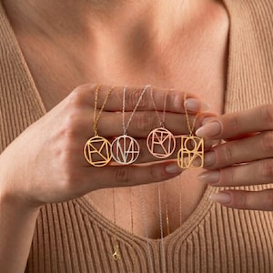 May include: Four geometric pendant necklaces in gold, silver, and rose gold tones. Each necklace features a different abstract design within a circular or square frame, suspended from delicate chains. The necklaces are held up by a person.