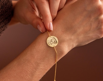 Könnte beinhalten: Ein goldfarbenes Armband mit einem runden Anhänger, der ein Haustierporträt und den Namen "Rosie" zeigt. Die feine Kette ist mit dem Anhänger verbunden. Das Armband wird am Handgelenk getragen.