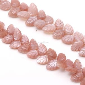 Peut inclure: Gros plan sur des perles de pierres précieuses pêche sculptées en forme de feuilles. Les perles, avec des veines détaillées, sont disposées en diagonale. La finition polie des pierres précieuses est visible sur fond blanc.