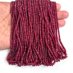 May include: A collection of multiple strands of small, faceted, deep red ruby gemstone beads. Each bead features a circular, flat disc shape with a polished, reflective surface, arranged in long, vertical strings of uniform size and color.