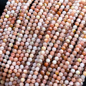 May include: Close-up of a collection of faceted, round beads in shades of peach, pink, and cream. The beads are strung together, creating a textured surface. Ideal for jewelry making, these beads offer a natural, earthy aesthetic.