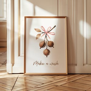 Puede incluir: Impresión artística enmarcada con una ilustración de acuarela de una rama con tres vainas marrones, hojas y un lazo rosa. Las palabras "Make a wish" están escritas en una fuente de guion debajo.