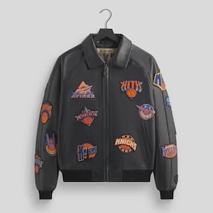 May include: A black leather jacket with multiple patches featuring basketball-related logos and text. The jacket has a collar, a zipper closure, and ribbed cuffs and hem. Patches include the text "Knicks" and "Kith".