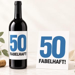 Op de afbeelding: Een donkere glazen wijnfles met een wit etiket met het grote blauwe getal 50 en de zwarte tekst FABELHAFT! naast een witte vierkante kaart met hetzelfde blauwe getal 50 en de zwarte tekst FABELHAFT! met een kurk ernaast geplaatst.