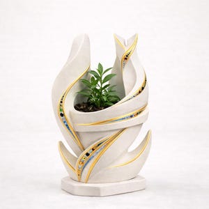 May include: A cream-coloured, abstract ceramic planter with a small green plant. The planter has a unique, flowing design with gold and jewel-toned accents. The base is a simple, geometric shape.