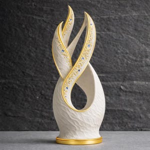 May include: A cream-coloured decorative sculpture with a textured surface and a gold base. The sculpture features intertwined, ribbon-like forms with gold trim and blue accents. The design is elegant and abstract, suitable for home decor.