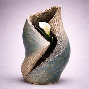 May include: A set of three ceramic mugs with a speckled, matte finish. The mugs are in shades of cream, light gray, and dark gray. Each mug has a simple, minimalist design and a rounded handle. The mugs are likely for coffee or tea.