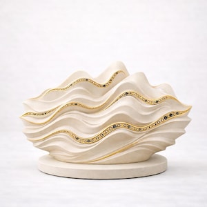 Pode incluir: Objeto decorativo em forma de onda, de cor creme, com detalhes dourados e pequenos adornos pretos. A escultura assenta numa base redonda, criando um design único e elegante. Provavelmente um artigo decorativo para casa ou escritório.