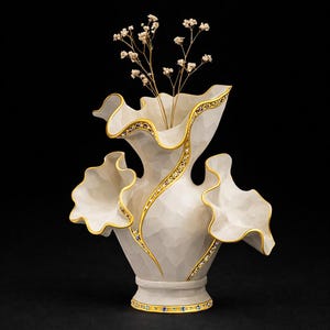 May include: A white ceramic vase with a textured surface, adorned with gold trim and small gemstones. The vase has a unique, ruffled design and holds delicate, dried flowers. The vase is a decorative home accent.